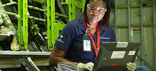 Woman with safety glasses and gloves working at a laptop computer