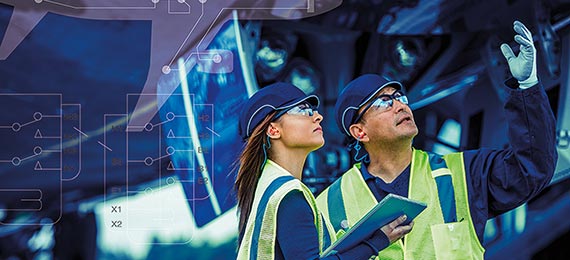 Two workers in bump caps, ear protection, high visiblity vests, and eye protection conducting an inspection